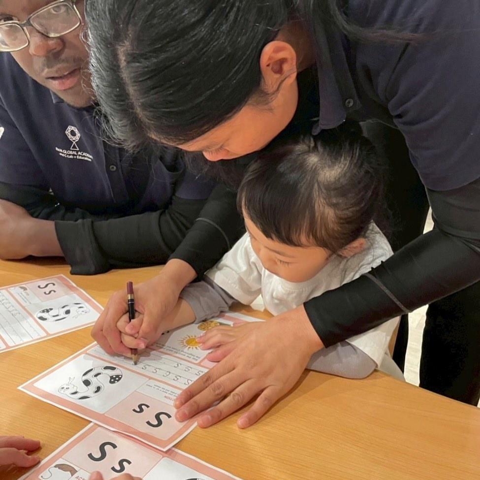 フォニックスのワークシートで「Ss」の文字を書く園児を、そばで見守り支える先生たち