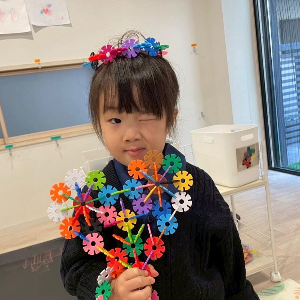 ブロックで作った王冠と大きな花を身につけ、得意げな表情を見せる園児