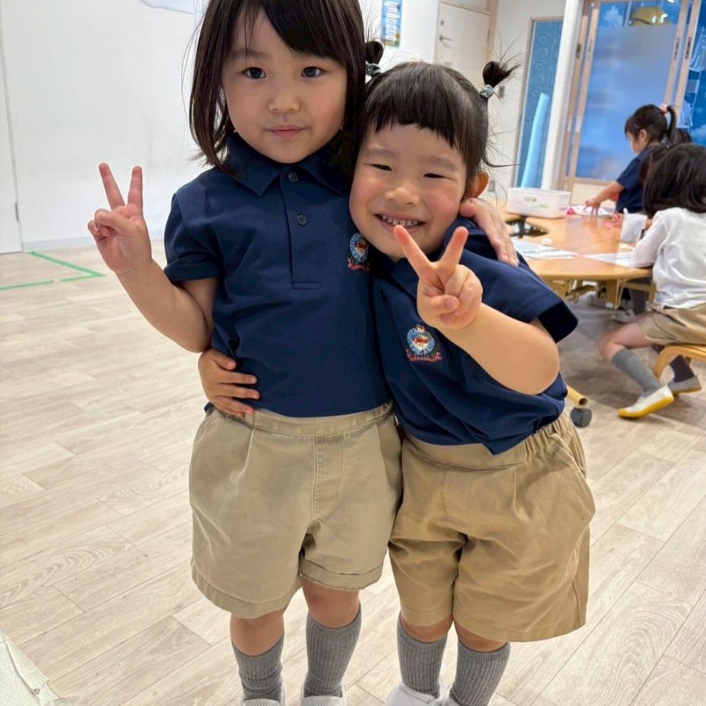 紺色のポロシャツの制服姿で肩を寄せ合い、笑顔でピースサインをする園児2名